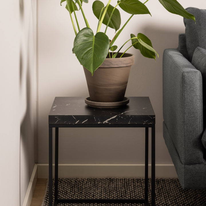 Barossa sidebord i sort marmorlook med sort metallramme, ved grå sofa med grønn plante