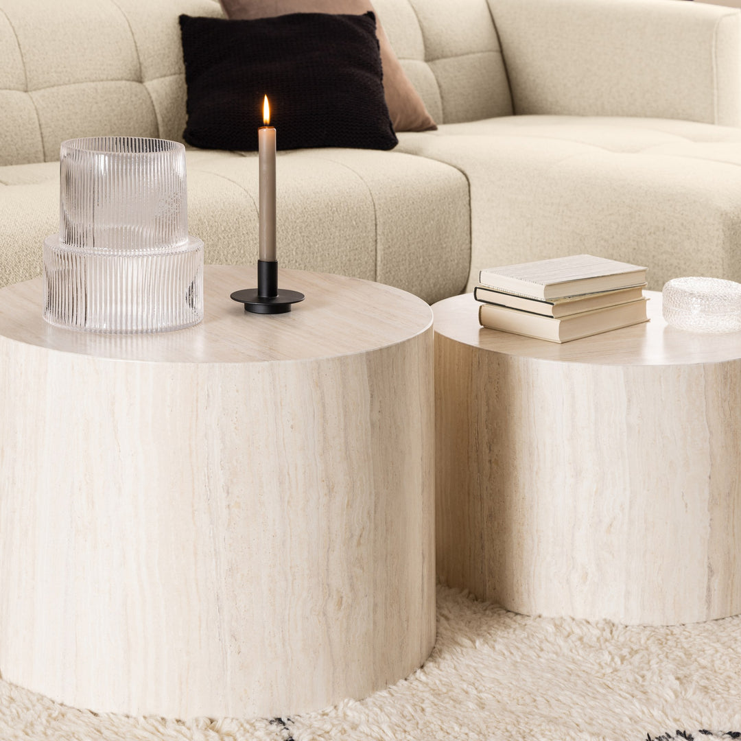 Dice sidebord, to beige travertinbord foran kremfarget bouclésofa med pute og lys