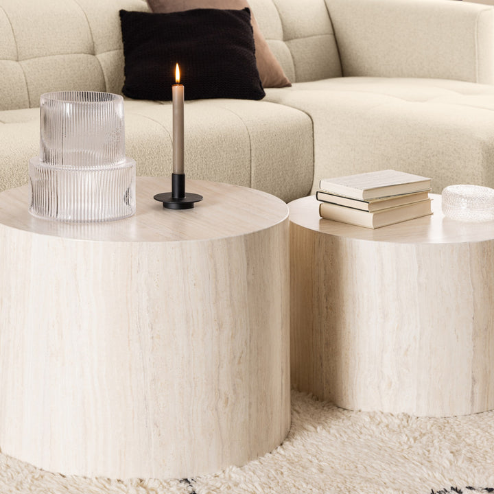 Dice sidebord, to beige travertinbord foran kremfarget bouclésofa med pute og lys
