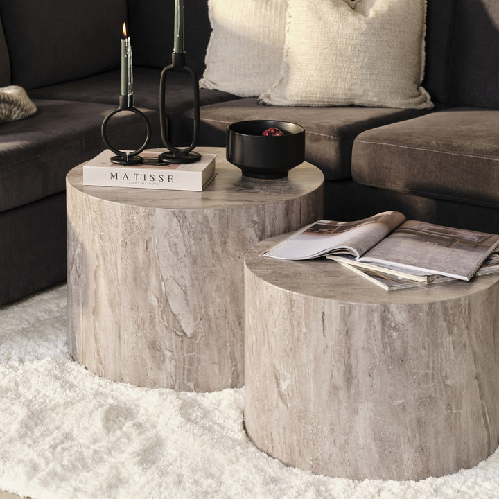 Dice sidebord i grå marmorlook, to runde bord med bøker og lysestaker ved mørk sofa