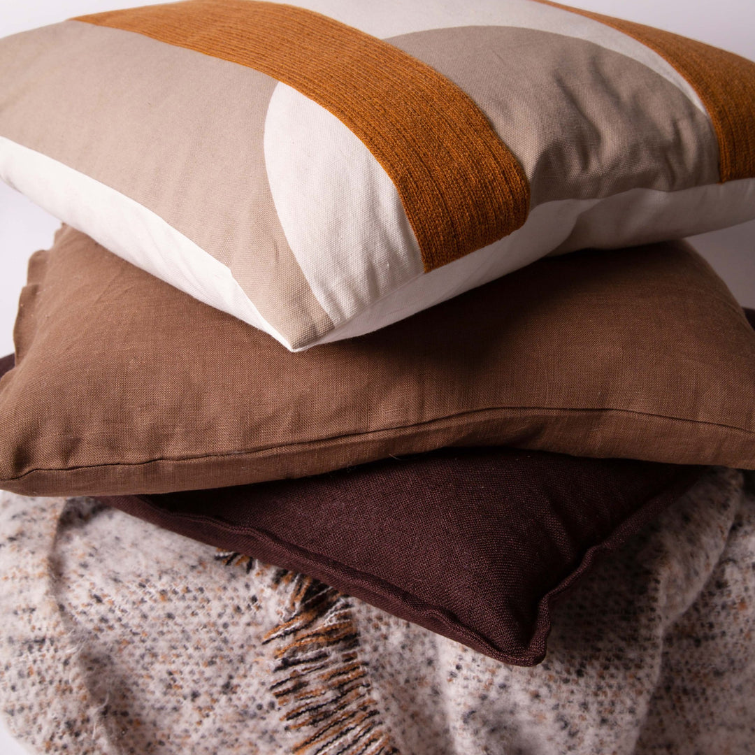 Dharma pyntepute med dun i krem, beige og rustbrunt, stablet på pynteputer i brun lin og ullpledd