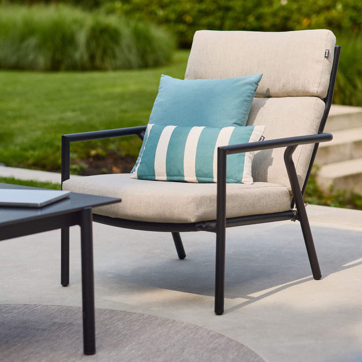 Hartman Shinzo loungestol i sort med beige puter og turkis stripepute på terrasse i hage
