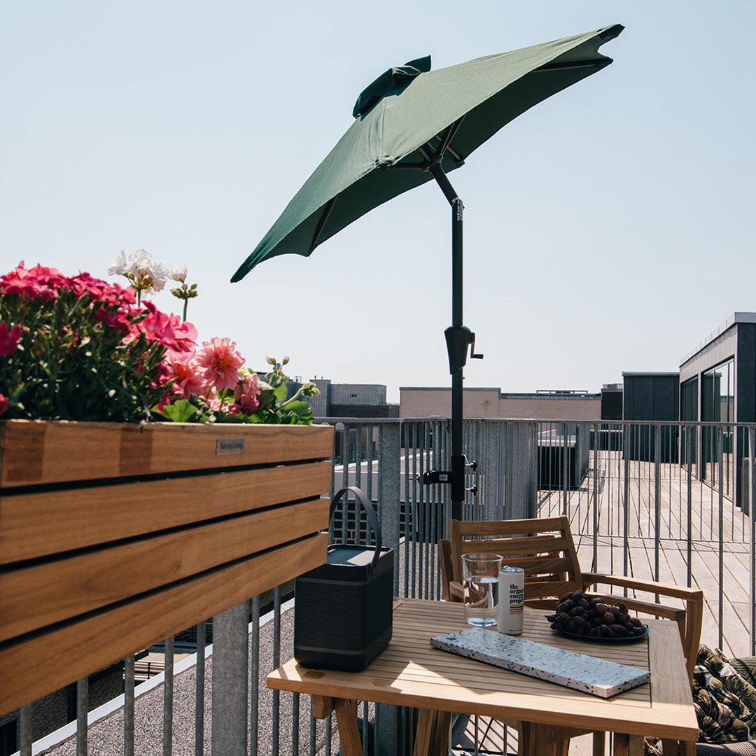 Parasollbeslag i matt sort på rekkverk, med grønn parasoll, blomsterkasse og kaffebord på terrasse