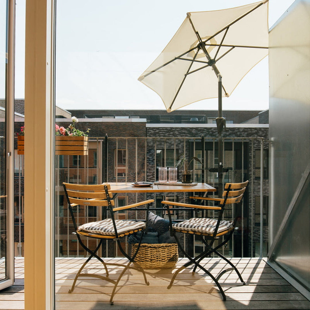 Parasollbeslag til balkong i bruk, kremhvit parasoll over bistrobord på solrik balkong
