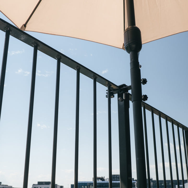 Parasollbeslag til balkong i matt sort som holder parasollstang på rekkverk mot blå himmel