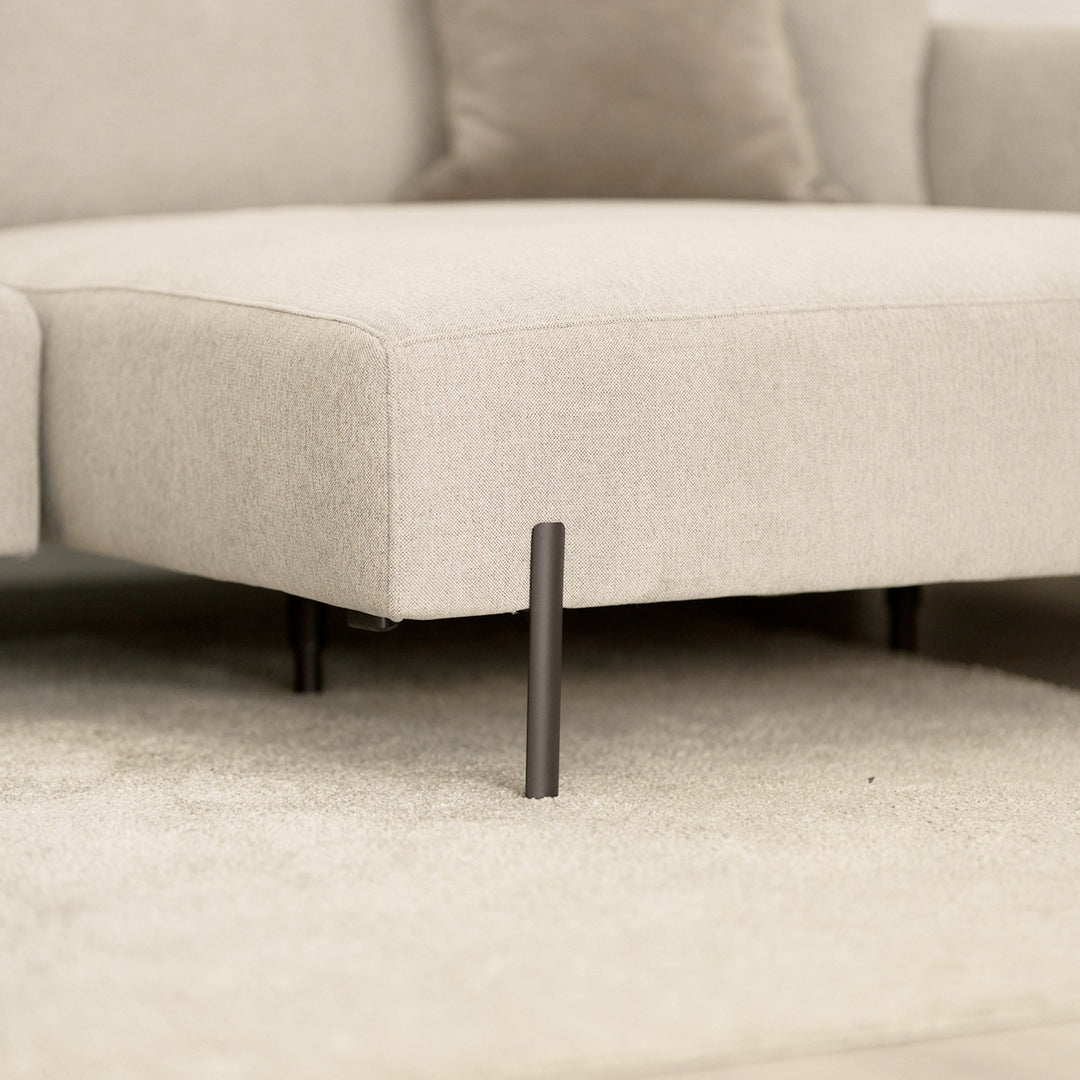 Milazzo hjørnesofa, nærbilde av sjeselong i lys beige stoff med sort metallben på lyst teppe