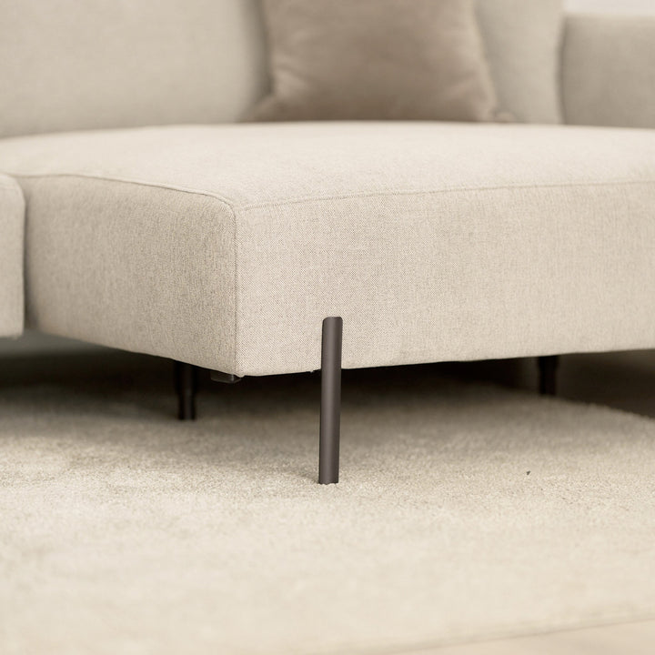 Milazzo hjørnesofa, nærbilde av sjeselong i lys beige stoff med sort metallben på lyst teppe