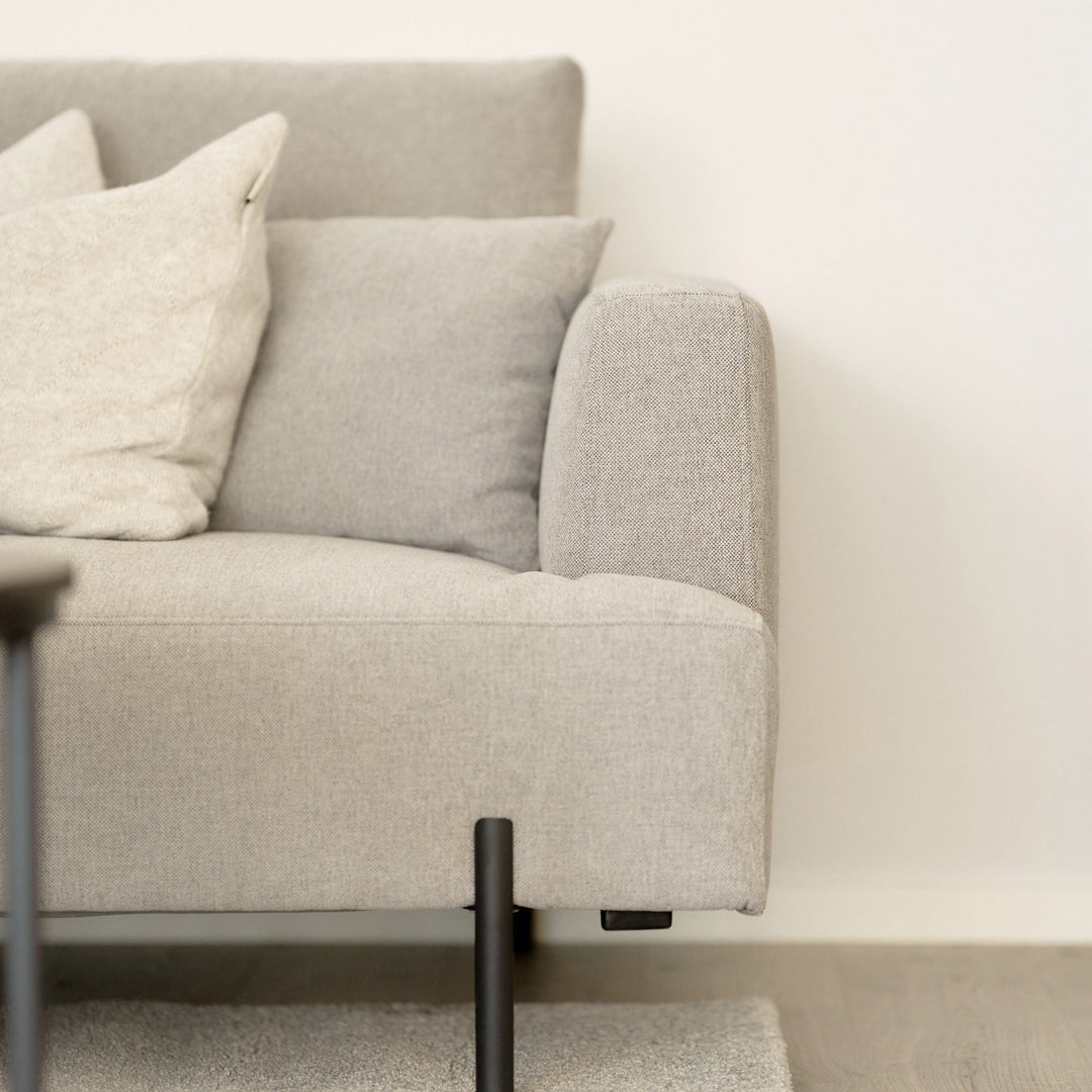 Milazzo hjørnesofa i nærbilde med lys beige stoff, avrundet armlene og lyse puter mot lys vegg