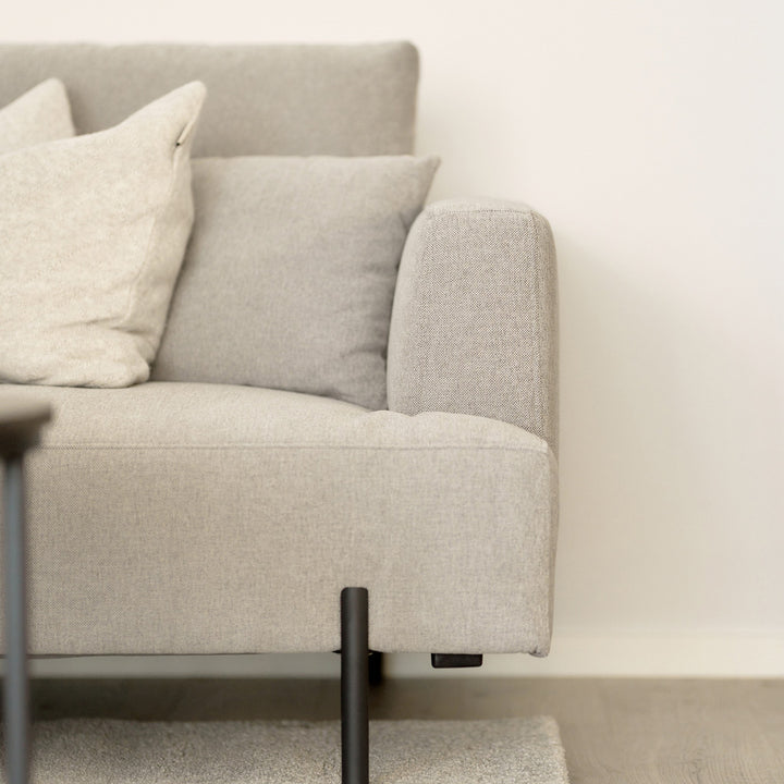 Milazzo hjørnesofa i nærbilde med lys beige stoff, avrundet armlene og lyse puter mot lys vegg