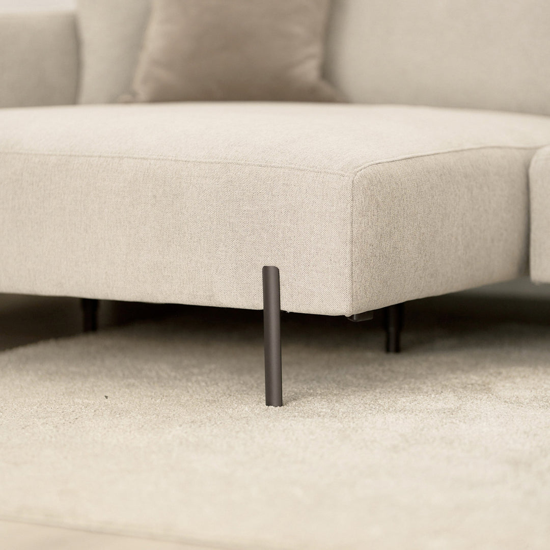Milazzo hjørnesofa, nærbilde av sete i lys beige stoff med sort metallben på lyst teppe