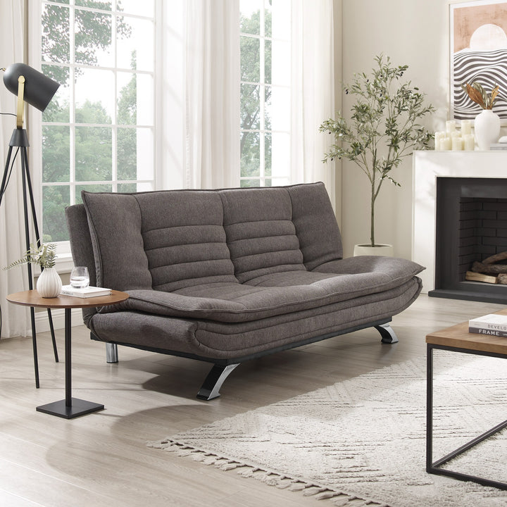 Friday sovesofa i mørk grå stoff, i lys stue med peis, kunstig tre og stativlampe