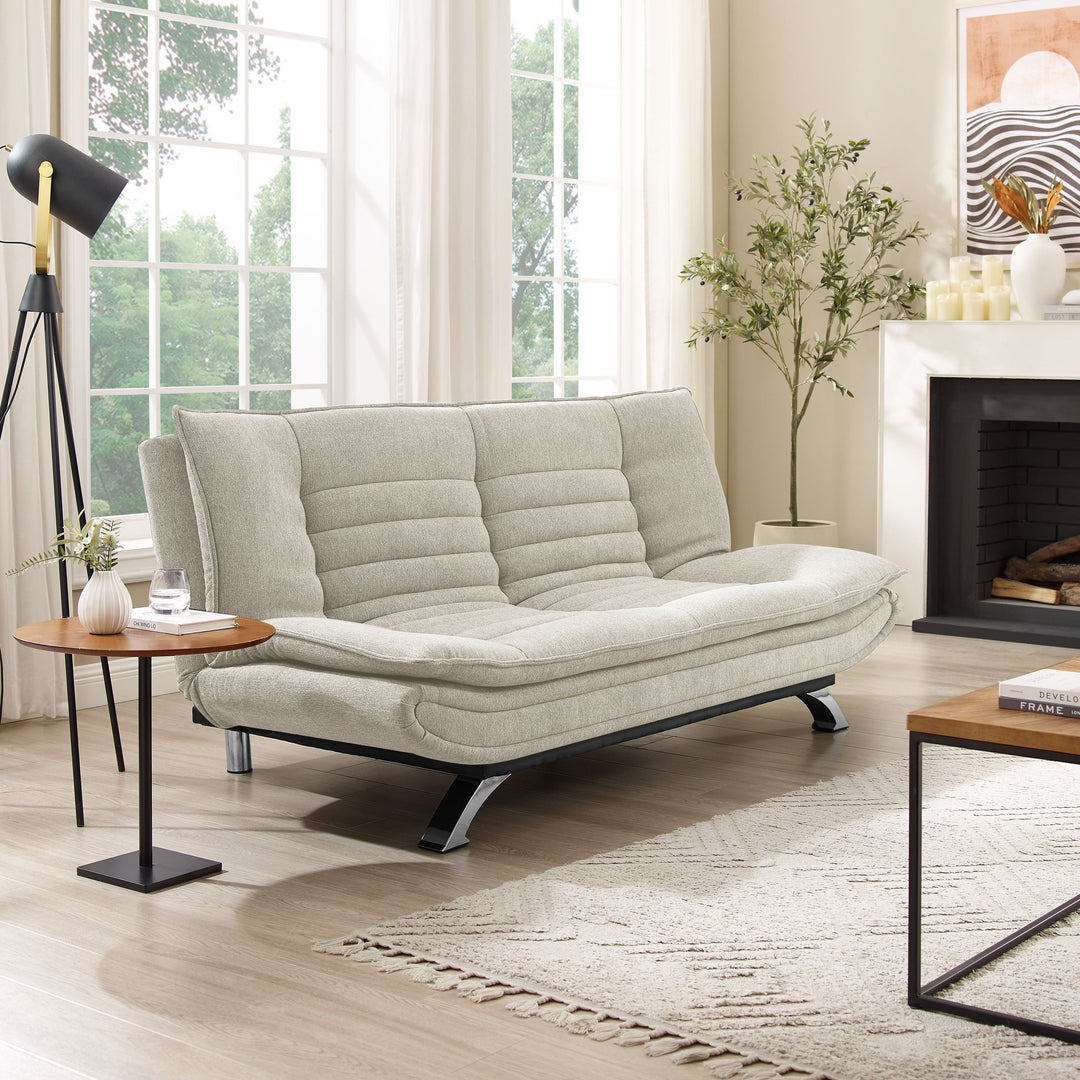 Friday sovesofa i lys beige stoff, i lys stue med peis, kunstig tre og stativlampe