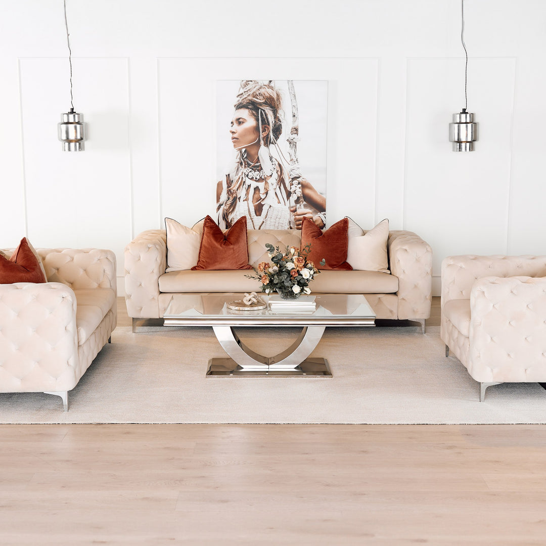 Bella sofa i kremfarget velur med knappetrekk, terrakotta puter, i lys stue med speilbord og portrettkunst