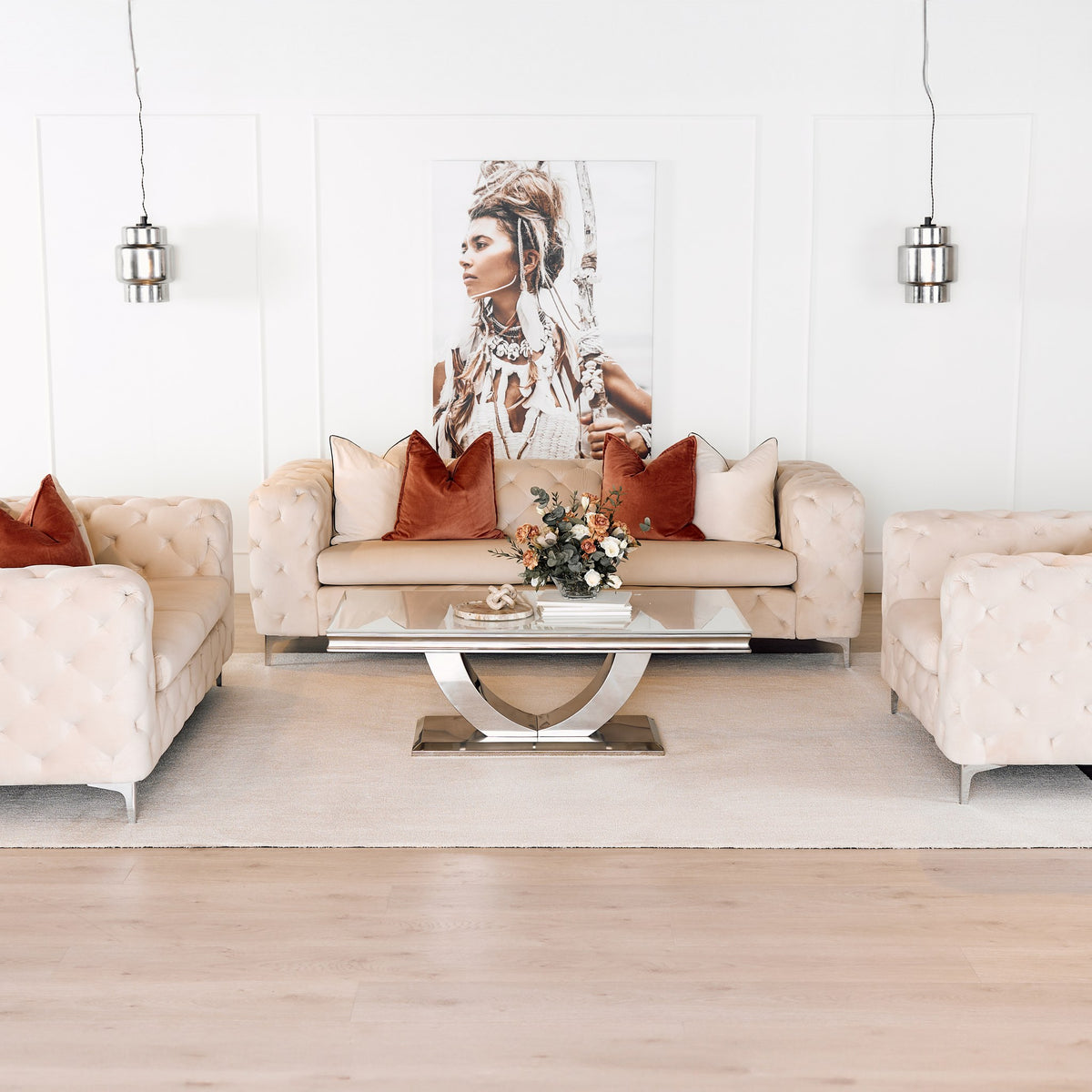 Bella sofa i kremfarget velur med knappetrekk, terrakotta puter, i lys stue med speilbord og portrettkunst