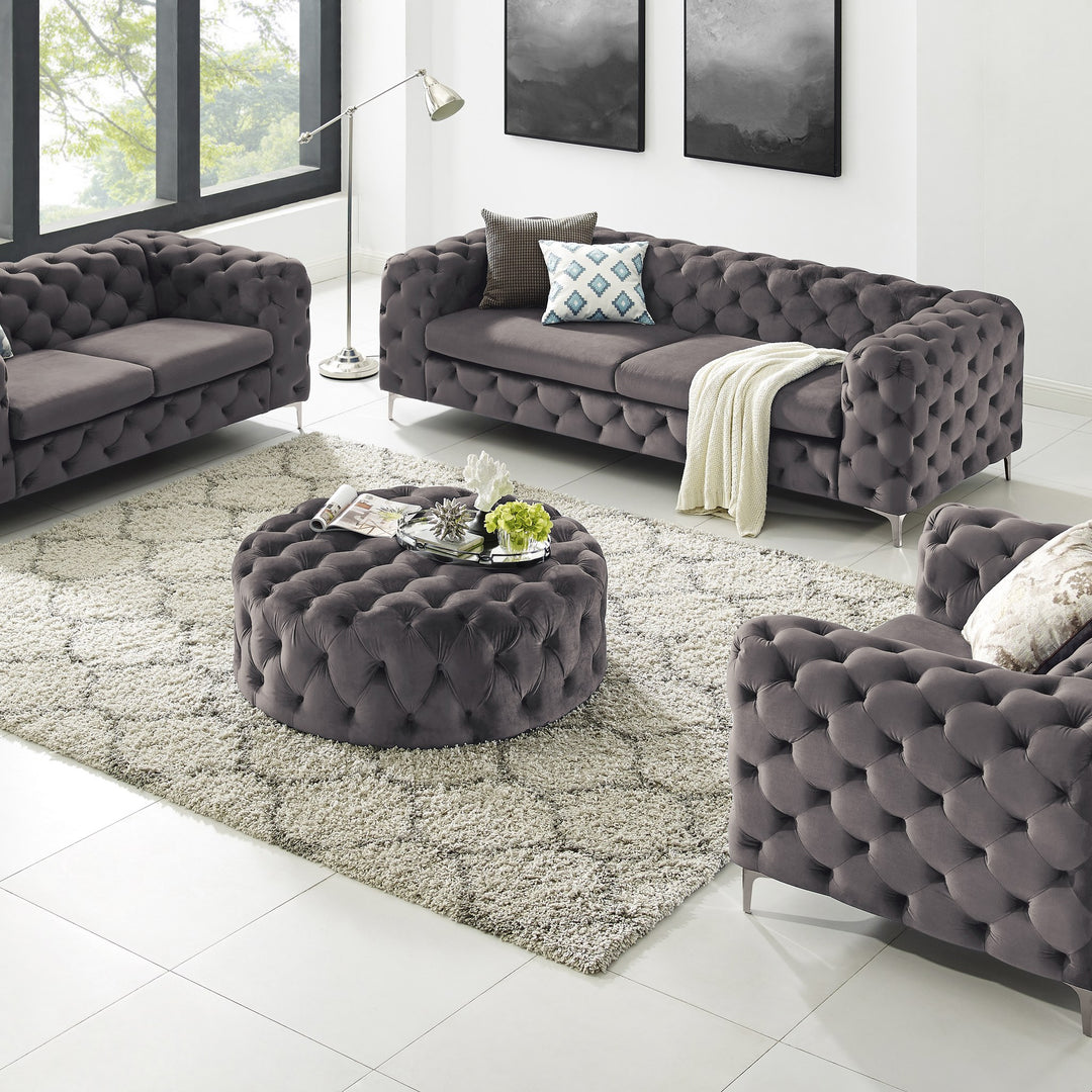 Bella sofa i grå tuftet velur med rund puff og lenestol, lyst stuerom med grått teppe.