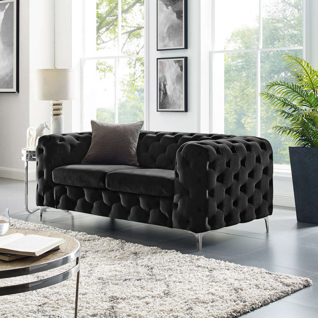 Bella sofa i sort velur med knappetrekk, i lys stue med shaggteppe, plante og bilder på vegg