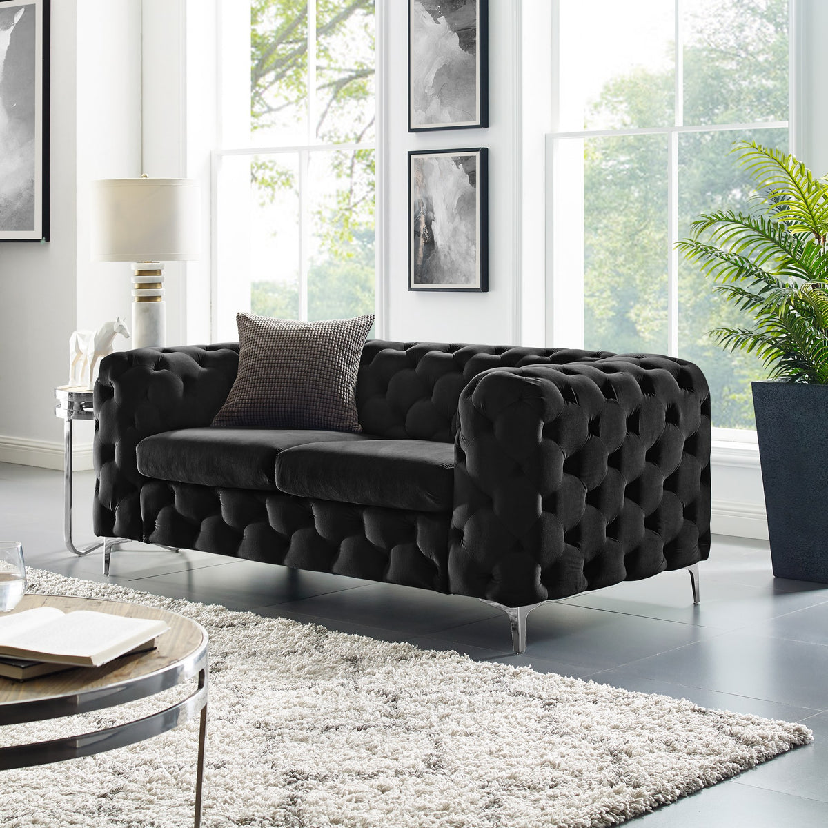 Bella sofa i sort velur med knappetrekk, i lys stue med shaggteppe, plante og bilder på vegg