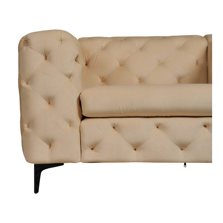 Bella sofa i beige tuftet velur med sorte ben, nærbilde av hjørne mot hvit bakgrunn.