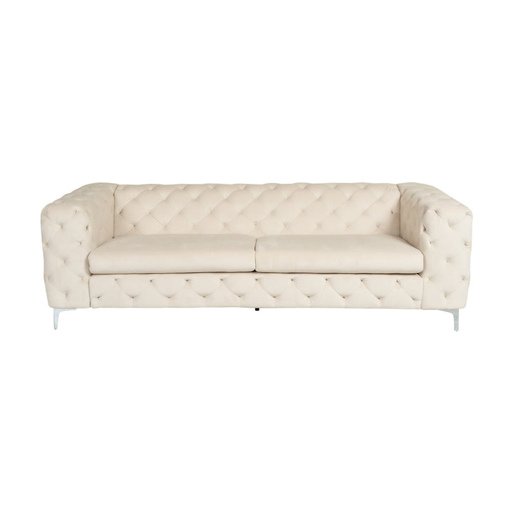Bella sofa i krem velur, treseter med dyp knapptufting og blanke krombein, sett forfra