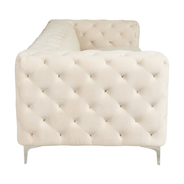 Bella sofa i krem velur, treseter med tuftet rygg og blanke krombein, sett fra siden