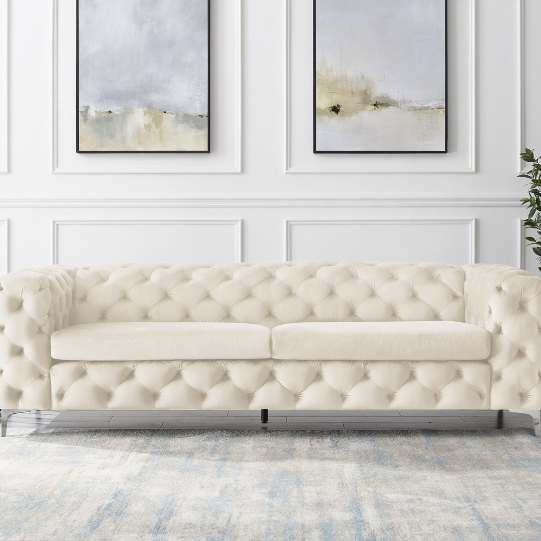 Bella sofa i kremhvit tuftet velur, panelvegg med abstrakt kunst og grønn plante.