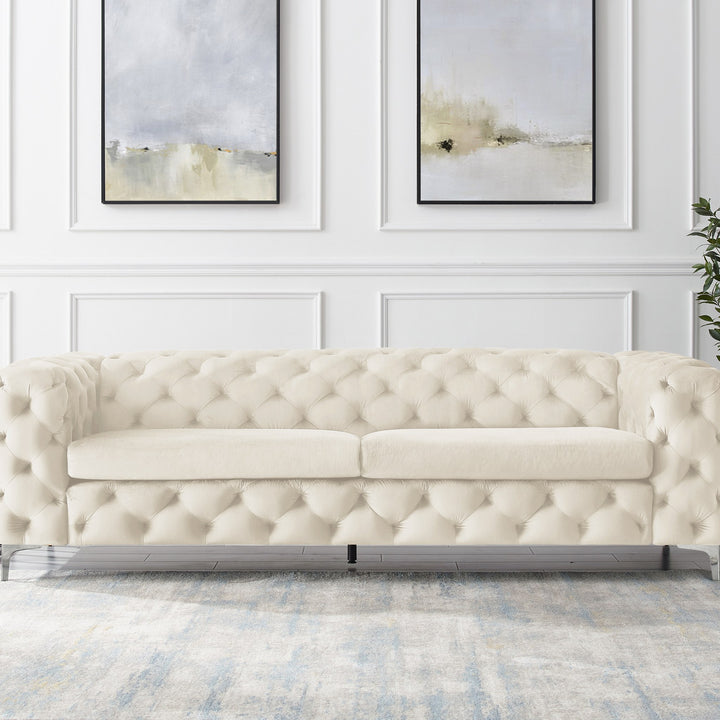 Bella sofa i kremhvit tuftet velur, panelvegg med abstrakt kunst og grønn plante.
