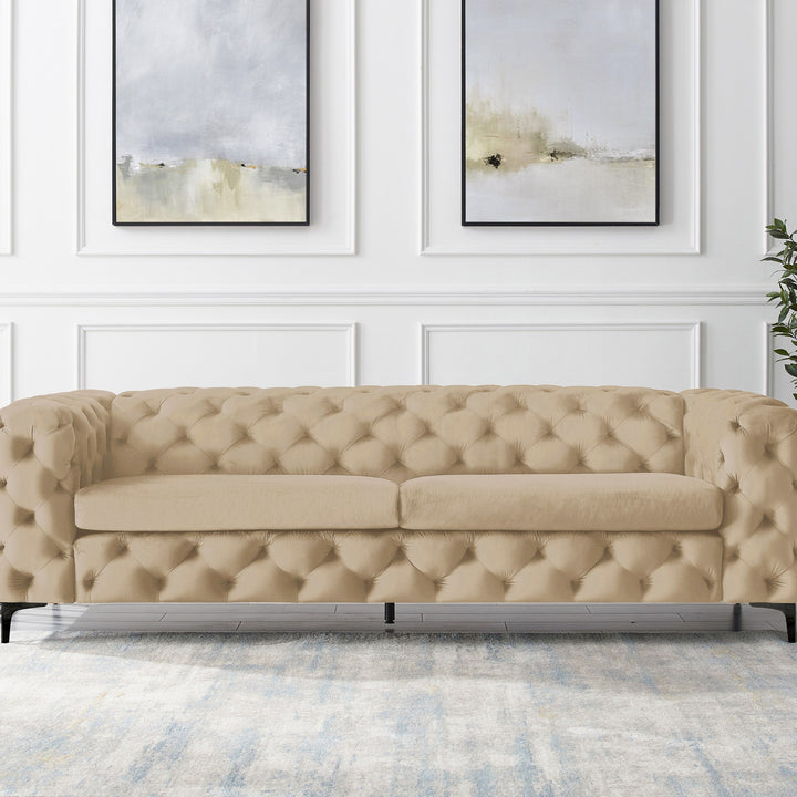 Bella sofa i beige tuftet velur, panelvegg med abstrakt kunst og grønn plante.