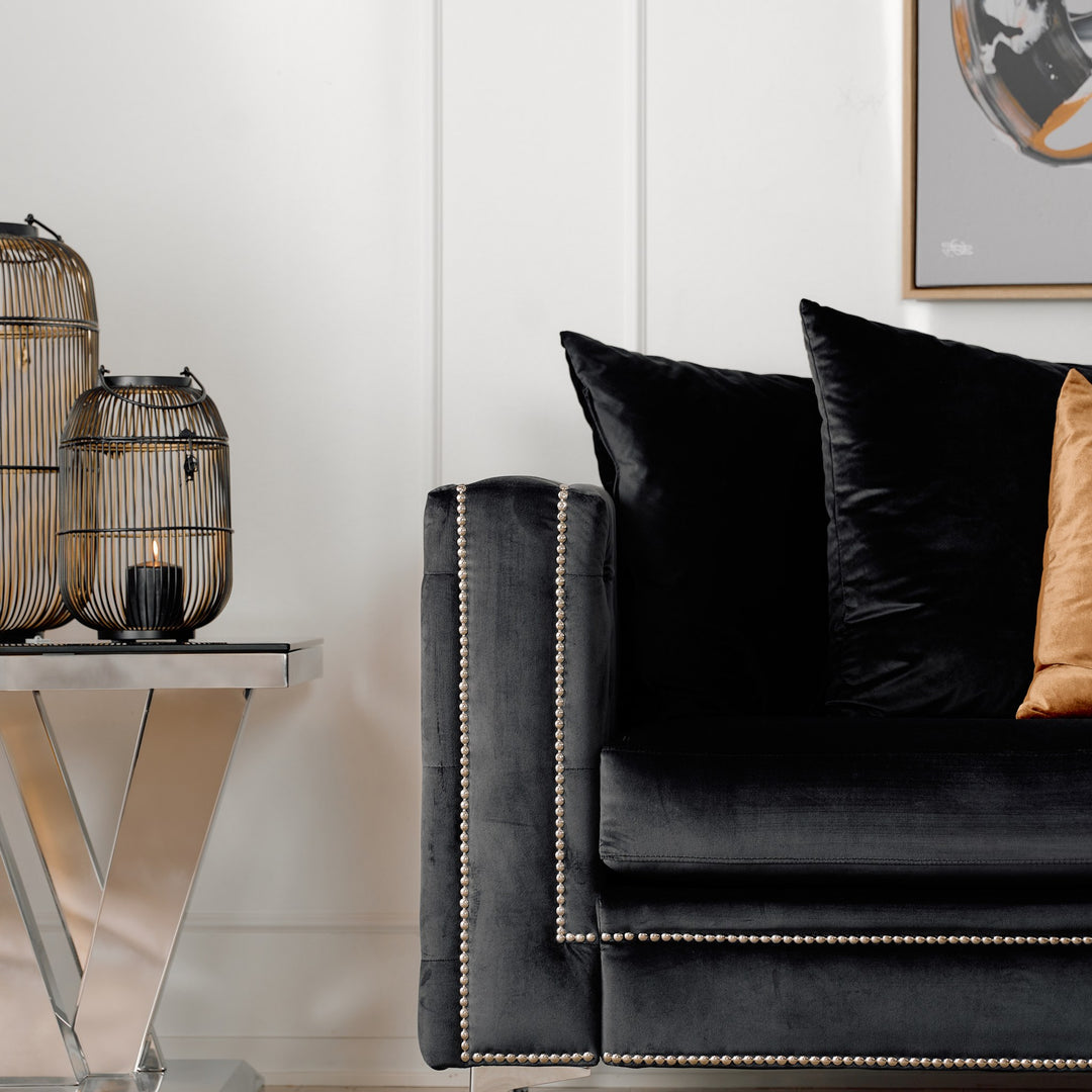 Dallas sofa i sort velur, nærbilde av tuftet arm med sølvnagler ved siden av dekorlykter