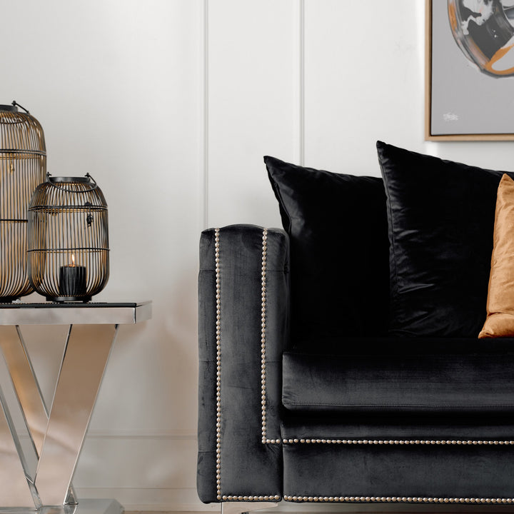 Dallas sofa i sort velur, nærbilde av tuftet arm med sølvnagler ved siden av dekorlykter