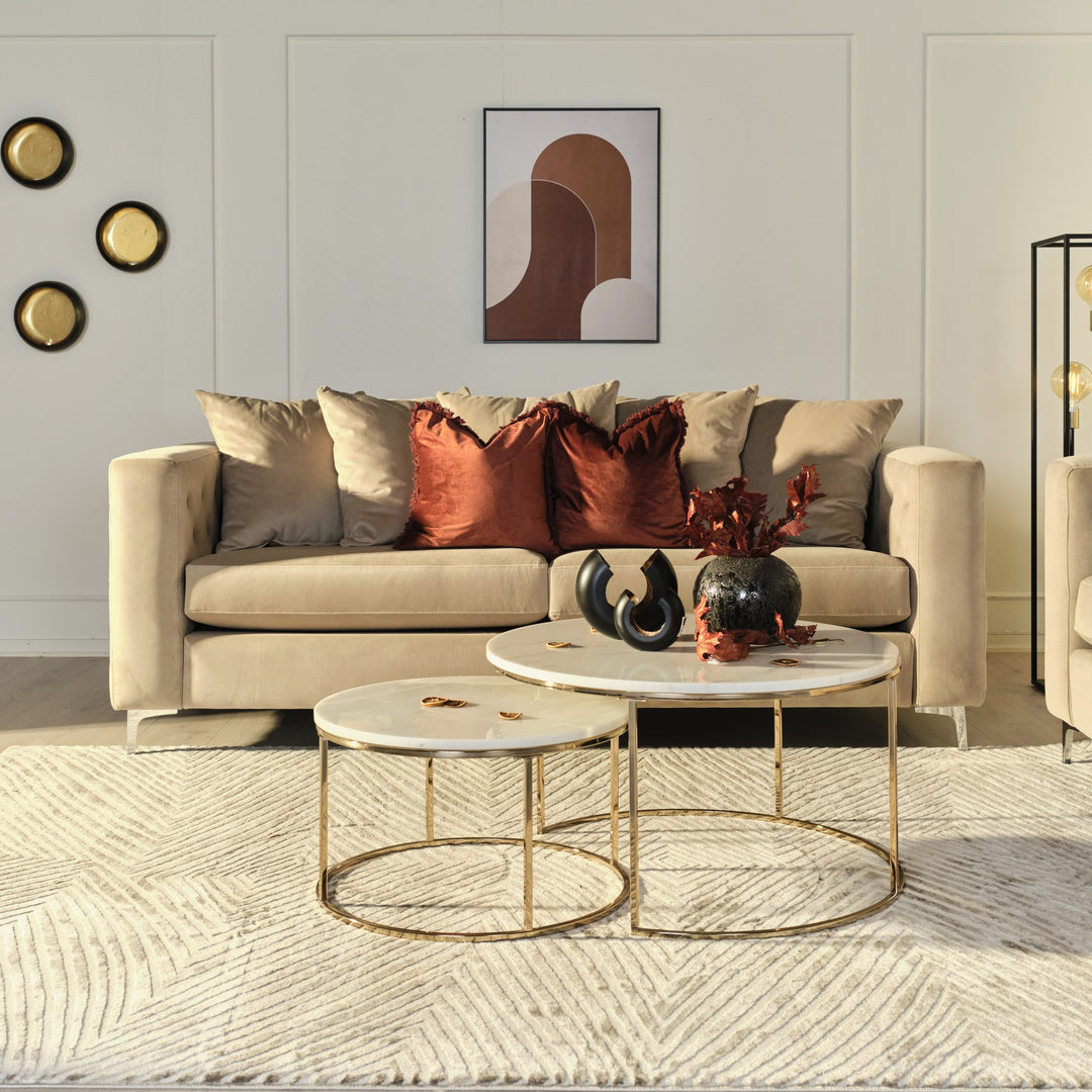Boston sofa i beige velur i lys stue, med rustrøde puter og gull- og marmorbord.