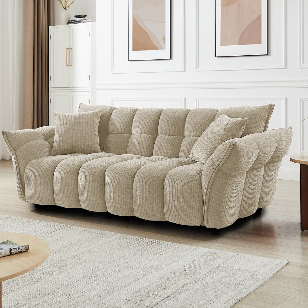 Marigold sofa i beige med puffet, ribbet design, i lys stue med abstrakte bilder.