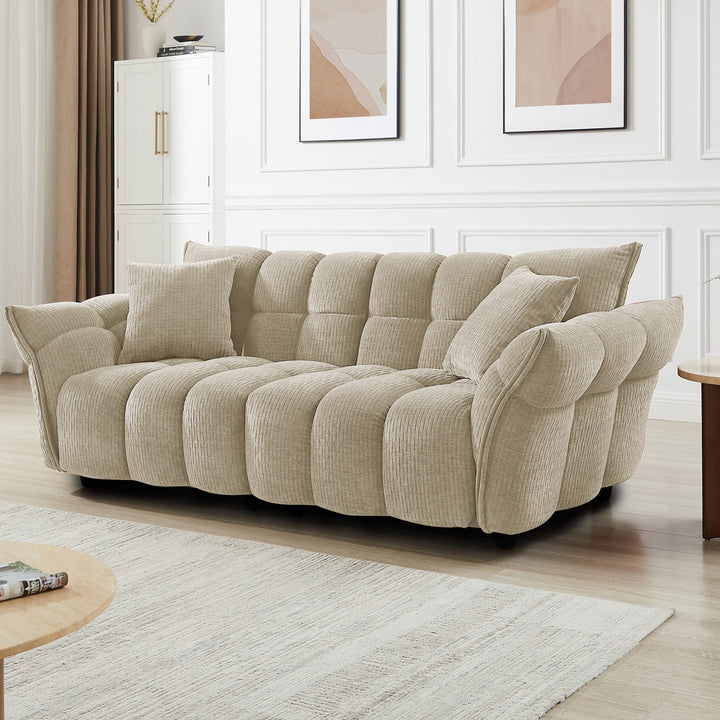 Marigold sofa i beige med puffet, ribbet design, i lys stue med abstrakte bilder.