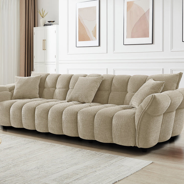 Marigold sofa i beige med puffet, ribbet design, i lys stue med abstrakte bilder.
