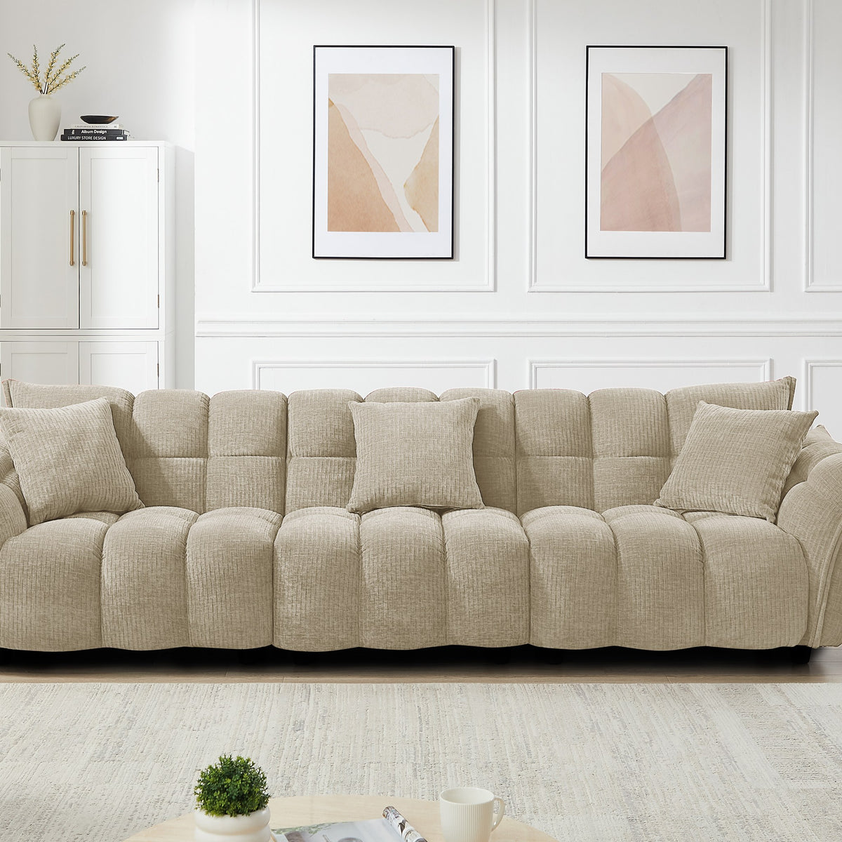Marigold sofa i beige kordfløyel, bred modell i stue med hvitt skap og abstrakte bilder