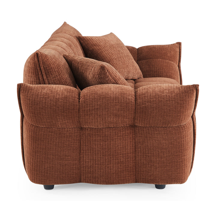 Marigold sofa i rustrødt sett fra siden, med puffet, ribbet design og mørke ben.