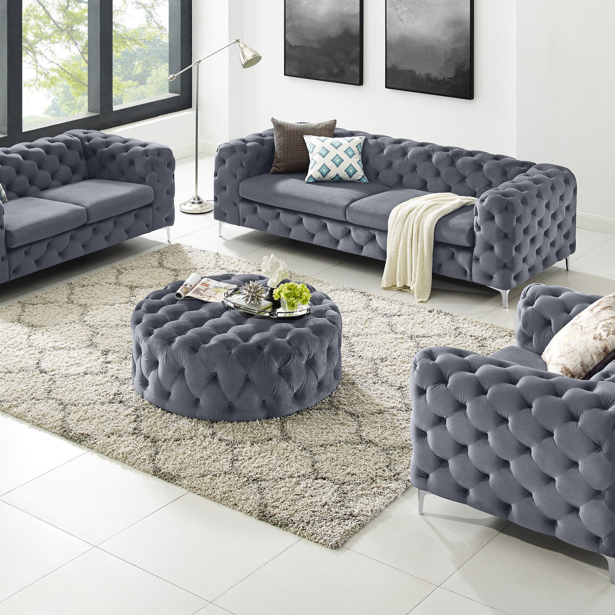 Bella puff i grå velur med knappetufting, rund modell i stue med chesterfieldsofaer og teppe