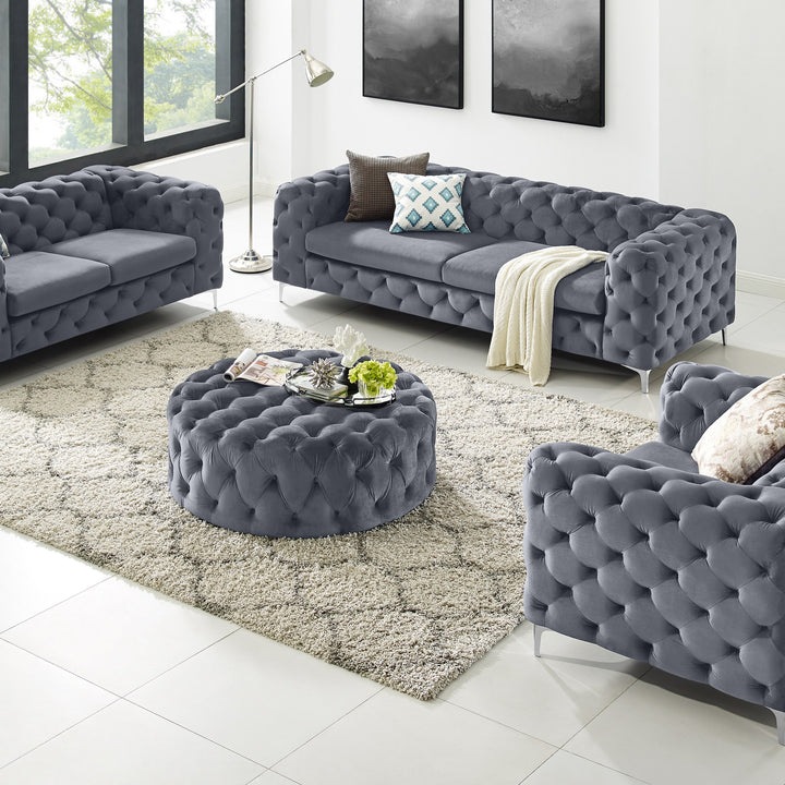 Bella puff i grå velur med knappetufting, rund modell i stue med chesterfieldsofaer og teppe