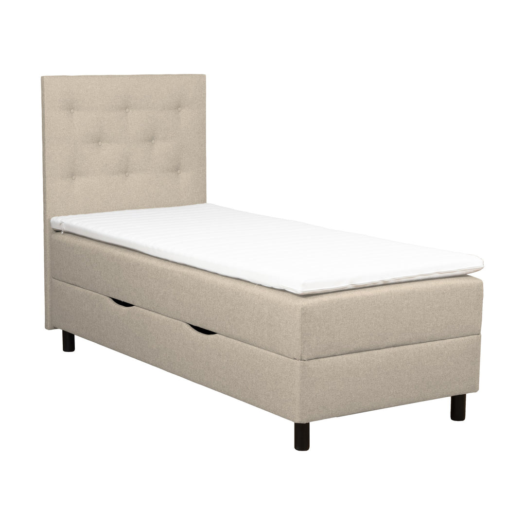 Rave HB1 sengegavl i beige, knappetuftet, vist med oppbevaringsseng og overmadrass.