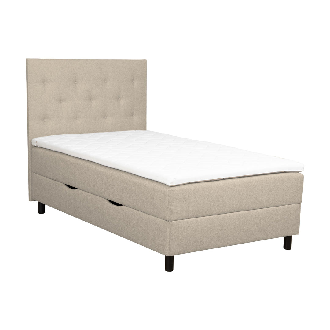 Rave HB1 sengegavl i beige, knappetuftet, vist med oppbevaringsseng og overmadrass.