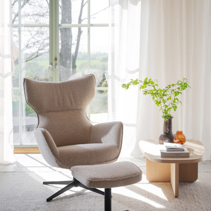 Rowico Jenkins lenestol i beige bouclé med fotskammel, ved vindu med plante og trebord