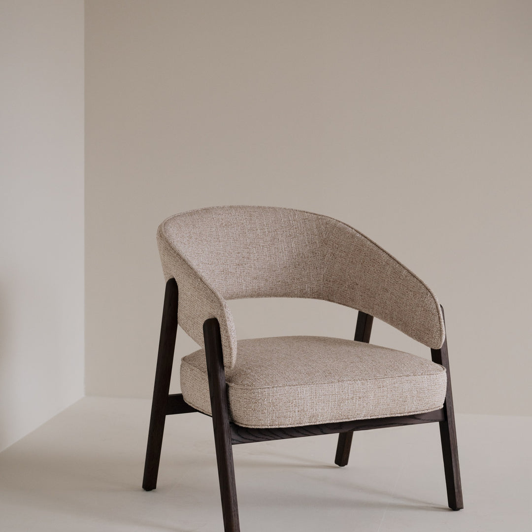 Rowico Barnaby loungestol i beige melert stoff og mørk eikeramme, plassert i et lyst, beige rom