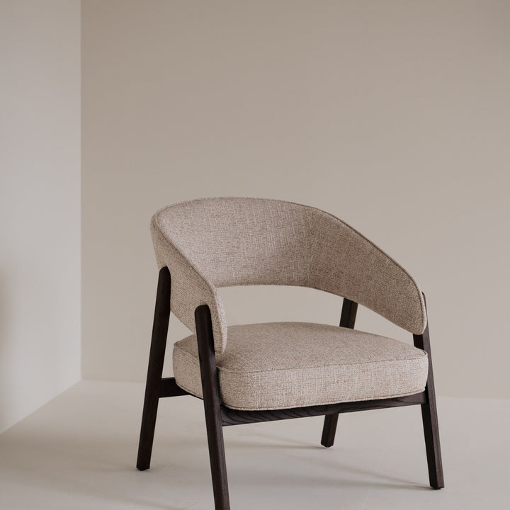 Rowico Barnaby loungestol i beige melert stoff og mørk eikeramme, plassert i et lyst, beige rom