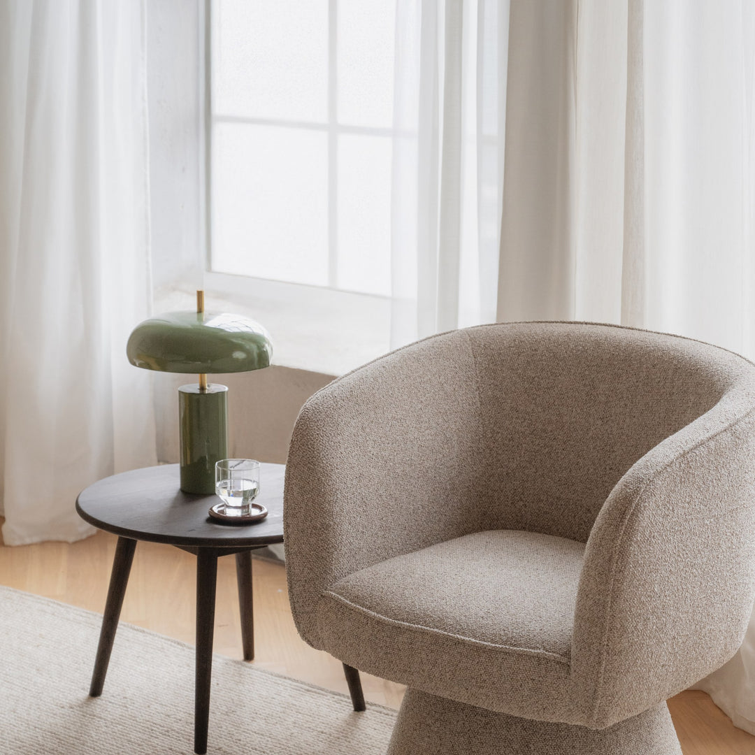 Rowico Shoreham loungestol i beige bouclé, ved sidebord med grønn lampe og lyse gardiner