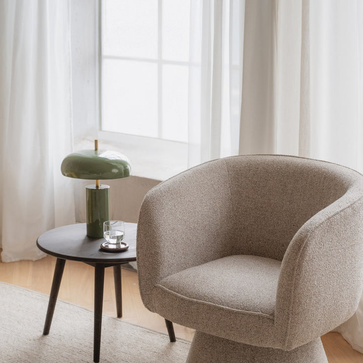 Rowico Shoreham loungestol i beige bouclé, ved sidebord med grønn lampe og lyse gardiner