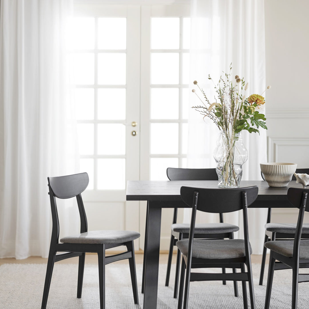 Rowico Winnipeg spisebord i sort eik med sorte stoler og glassvase ved lyse vinduer