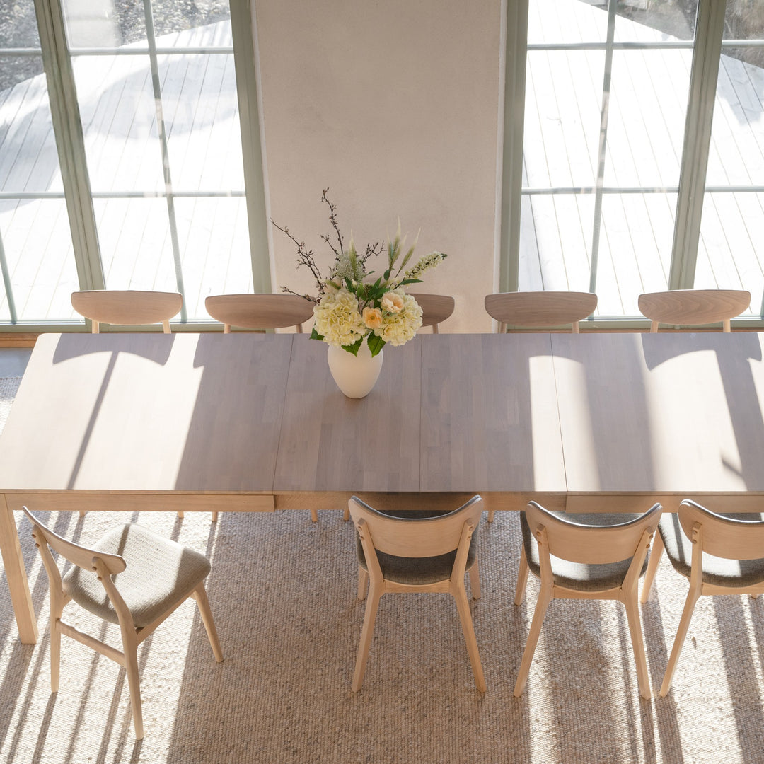 Rowico Gardner tilleggsplate i hvitpigmentert eik, lyst spisebord ovenfra med lyse stoler og blomstervase