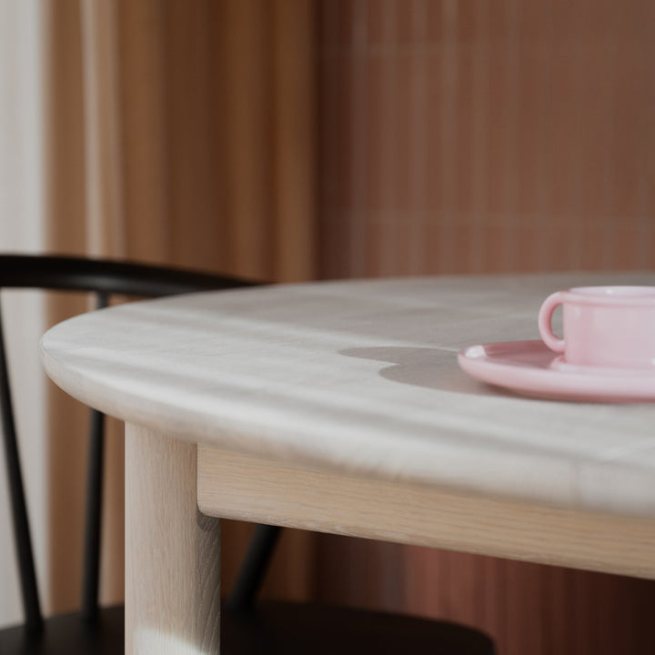 Rowico Derrymore rundt spisebord i hvitpigmentert eik, nærbilde med rosa kopp og sort stol.