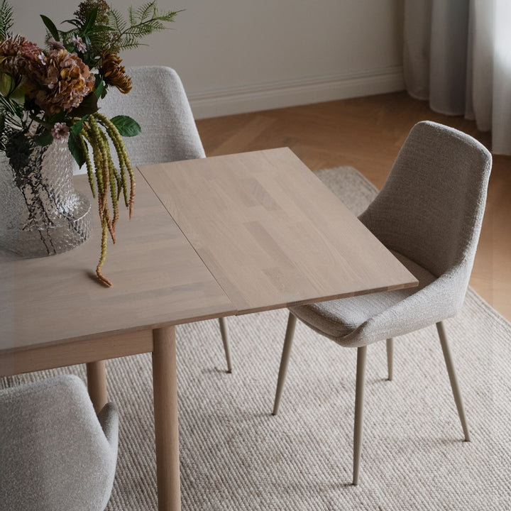 Rowico Derrymore spisebord i hvitpigmentert eik ovenfra med tørkede blomster, beige boucléstoler og teppe