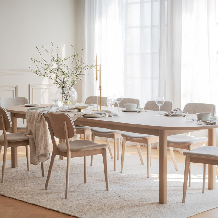 Rowico Gifford spisebord i lys eik med lyse stoler i solfylt spiserom med blomstergren