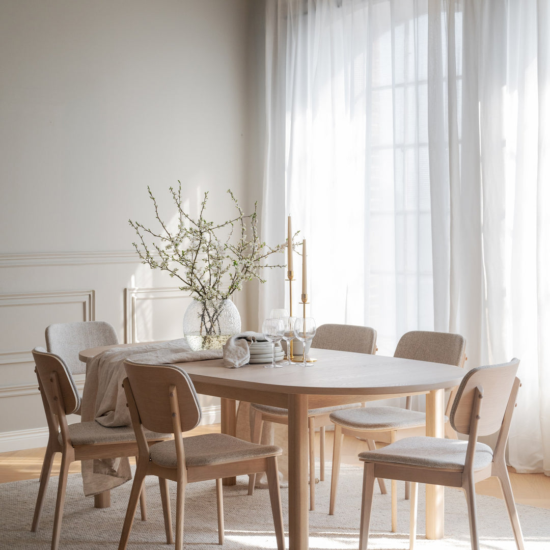 Rowico Gifford spisebord i hvitpigmentert eik i lyst spiserom med lyse stoler, blomstrende grener og lysestaker
